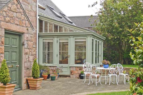 Sage green lean-to conservatory against a Jersey granite house